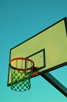 A nostalgic close-up of a basketball hoop with vintage style against a clear blue sky.
