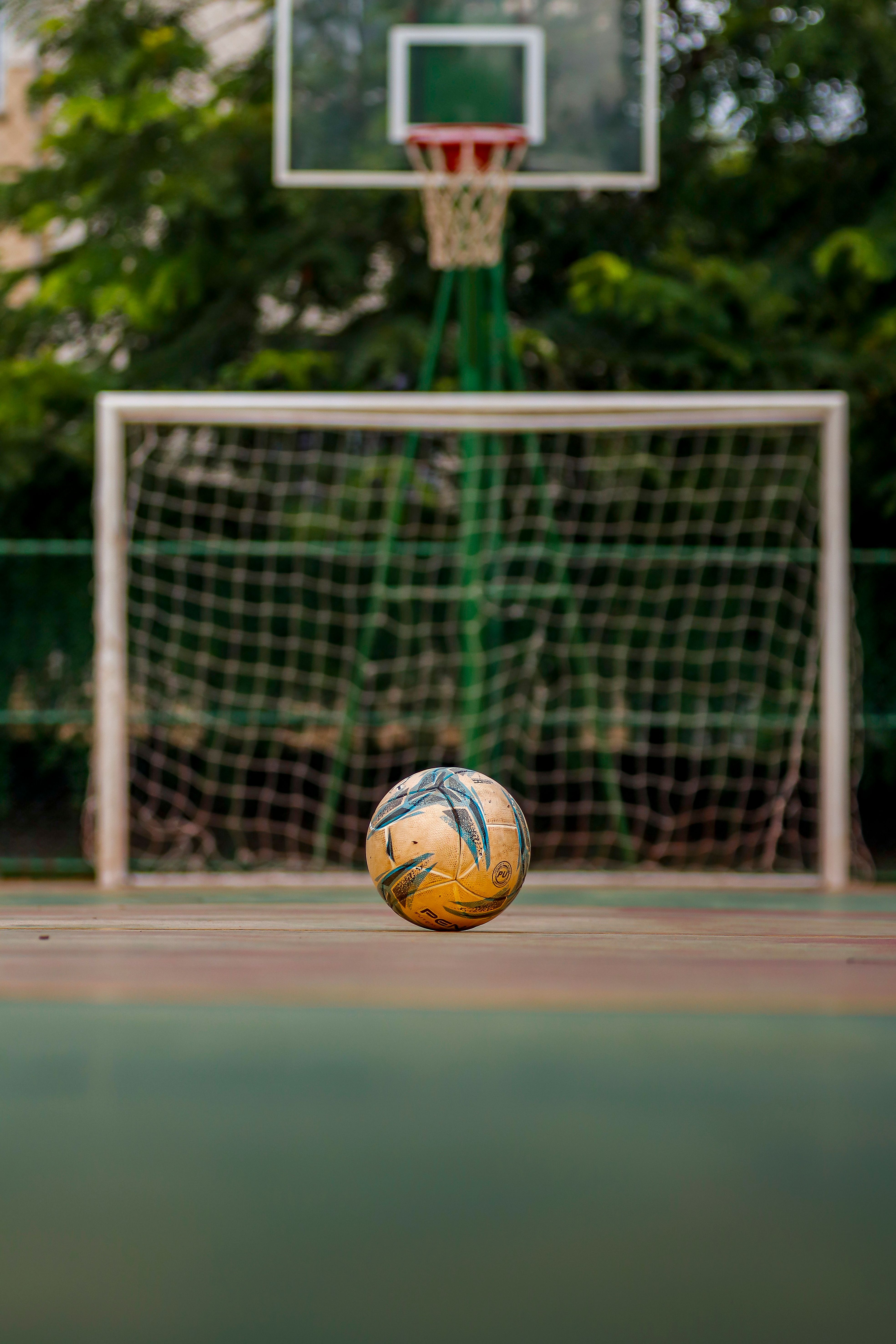 Soccer ball on a deserted court with both soccer goal and basketball hoop in view, outdoors.