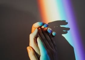 Artistic representation of unity with hands holding under colorful rainbow light reflection.