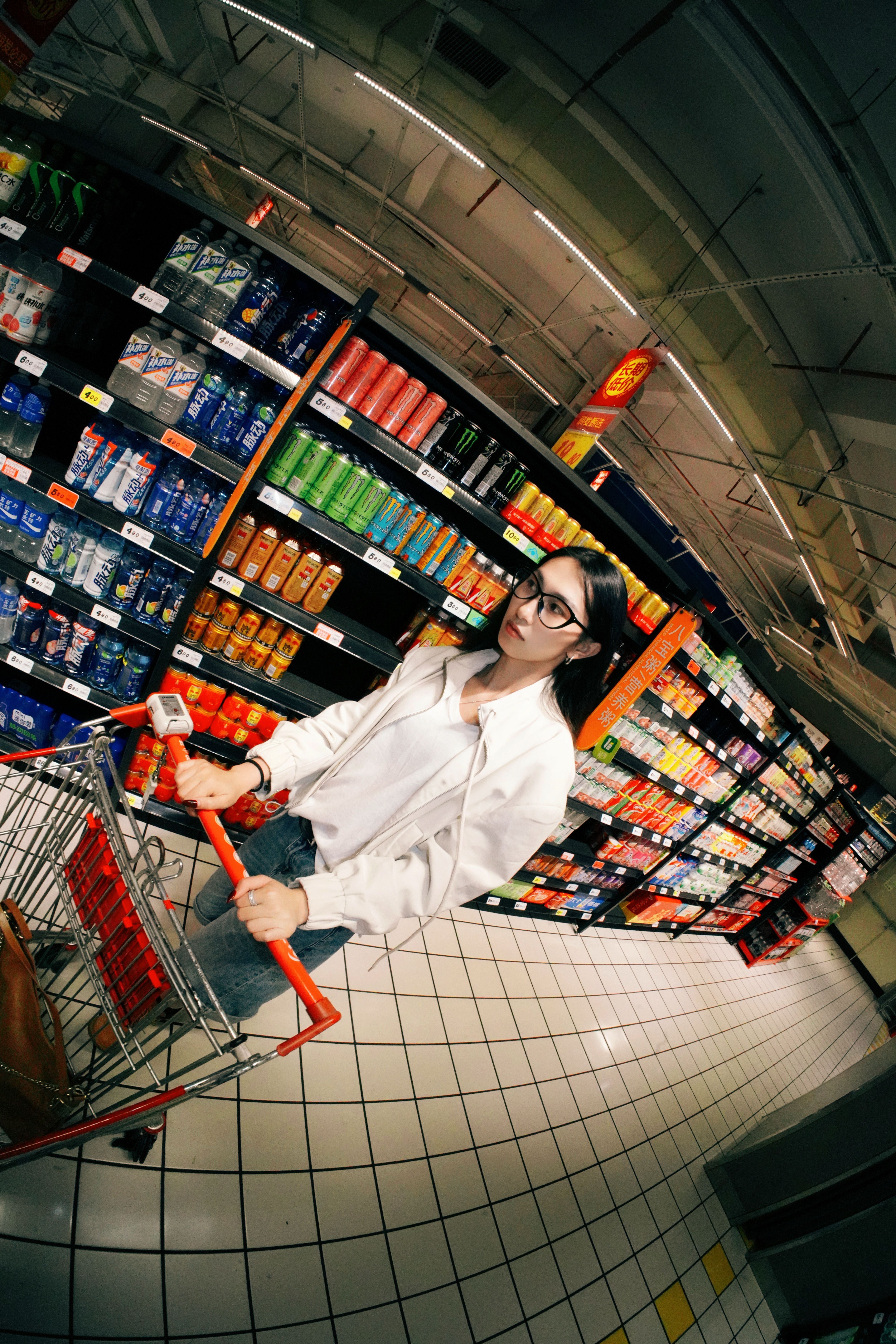 Young woman shopping in a well-stocked grocery aisle, pushing a cart and browsing products.