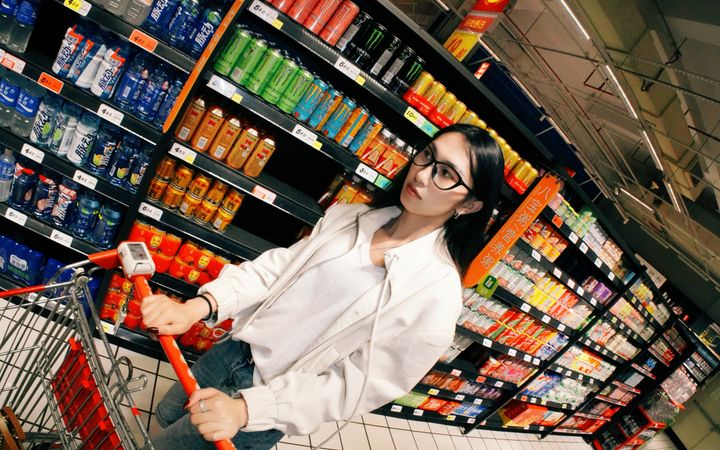 Young woman shopping in a well-stocked grocery aisle, pushing a cart and browsing products.