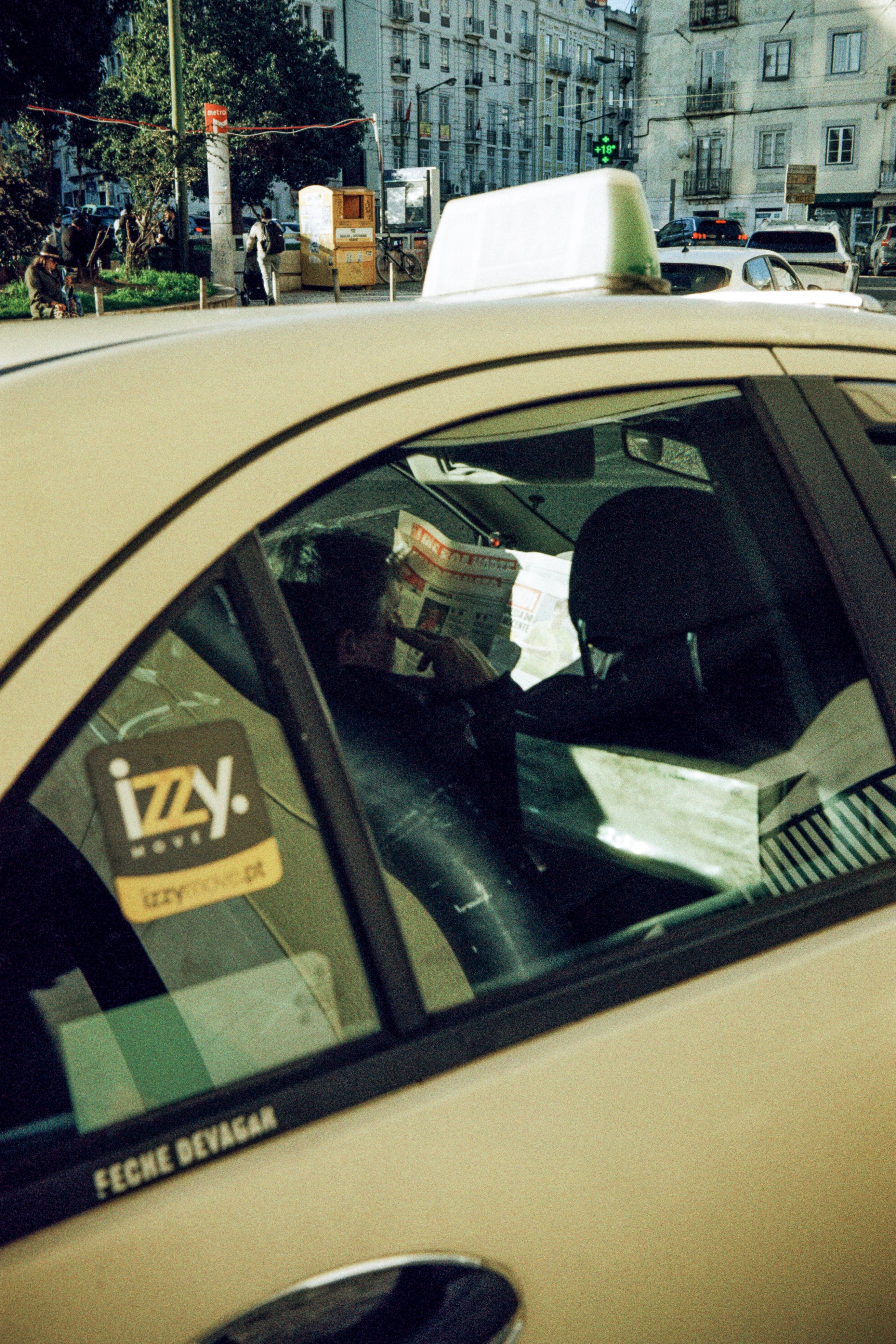 A taxi scene in Lisbon with a passenger reading a newspaper inside the cab.