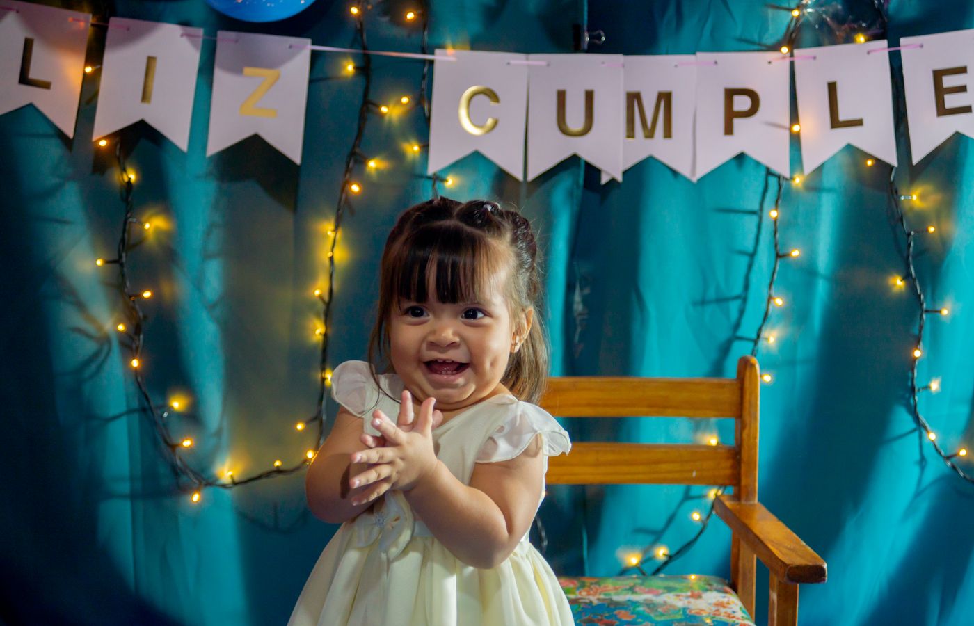 Adorable baby clapping at a birthday celebration with festive lights.