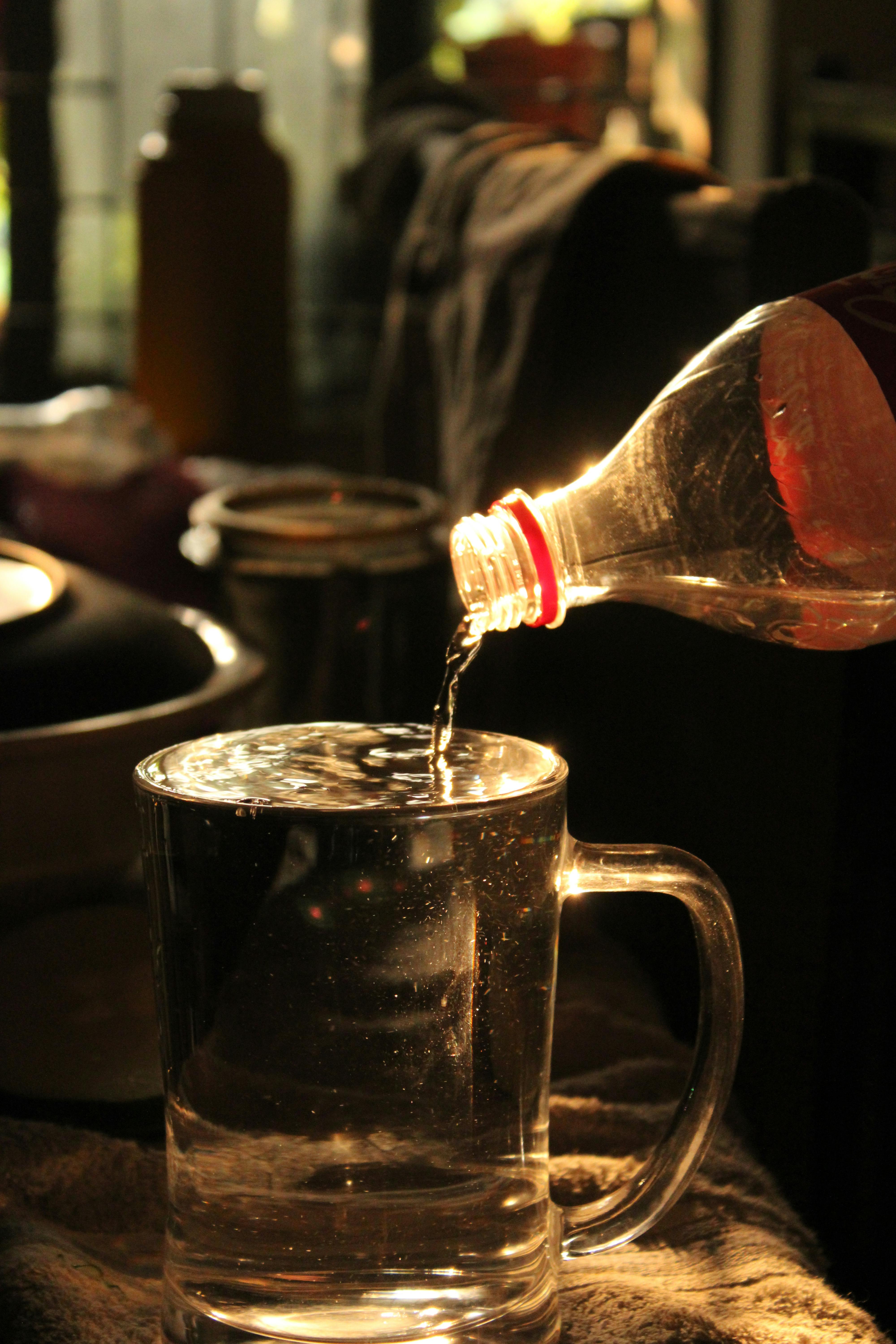 Sunlight casts a warm glow as water is poured from a bottle into a glass mug indoors.