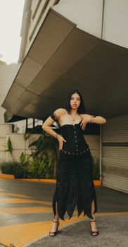 Fashionable woman in black dress posing confidently outdoors with modern architecture background.