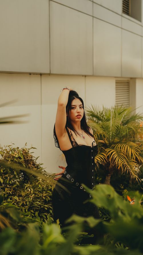 Free Stylish woman poses confidently in an outdoor urban garden, showcasing modern fashion in a natural setting. Stock Photo