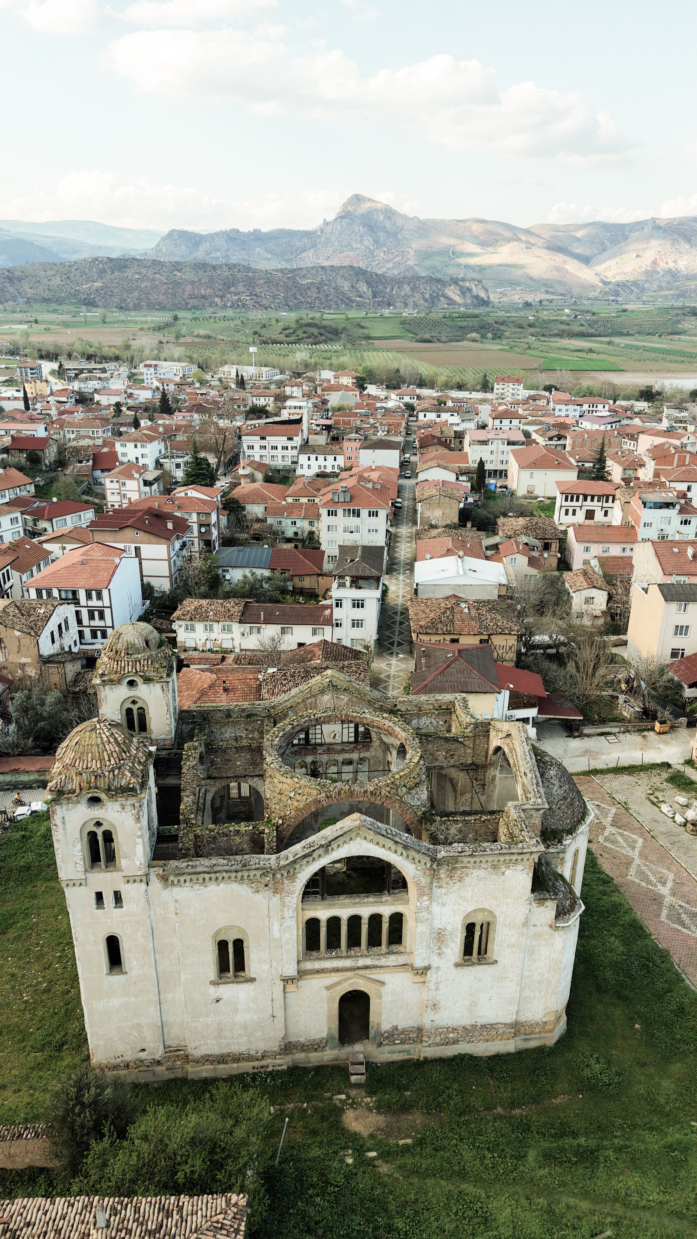 A stunning aerial shot of ancient ruins amidst a quaint town with mountainous backdrop.