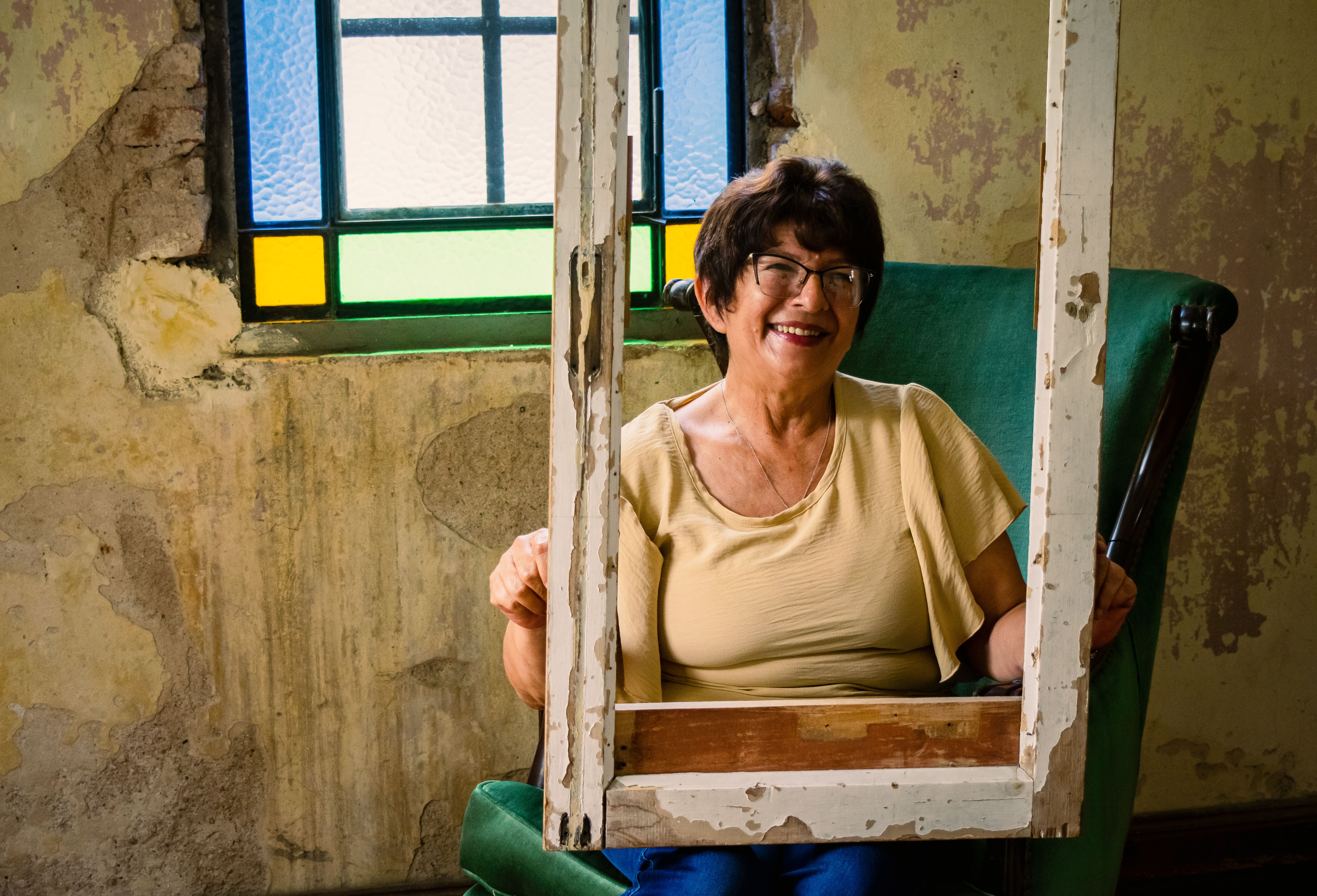 Cheerful woman sitting in a vintage setting with stained glass window and rustic decor.