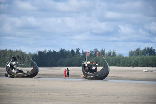 Free Fishing boats and people on a sandy beach under a cloudy sky. Stock Photo