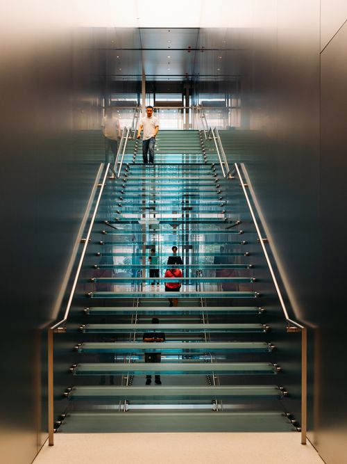Free Contemporary glass staircase with people ascending, showcasing modern architecture indoors. Stock Photo