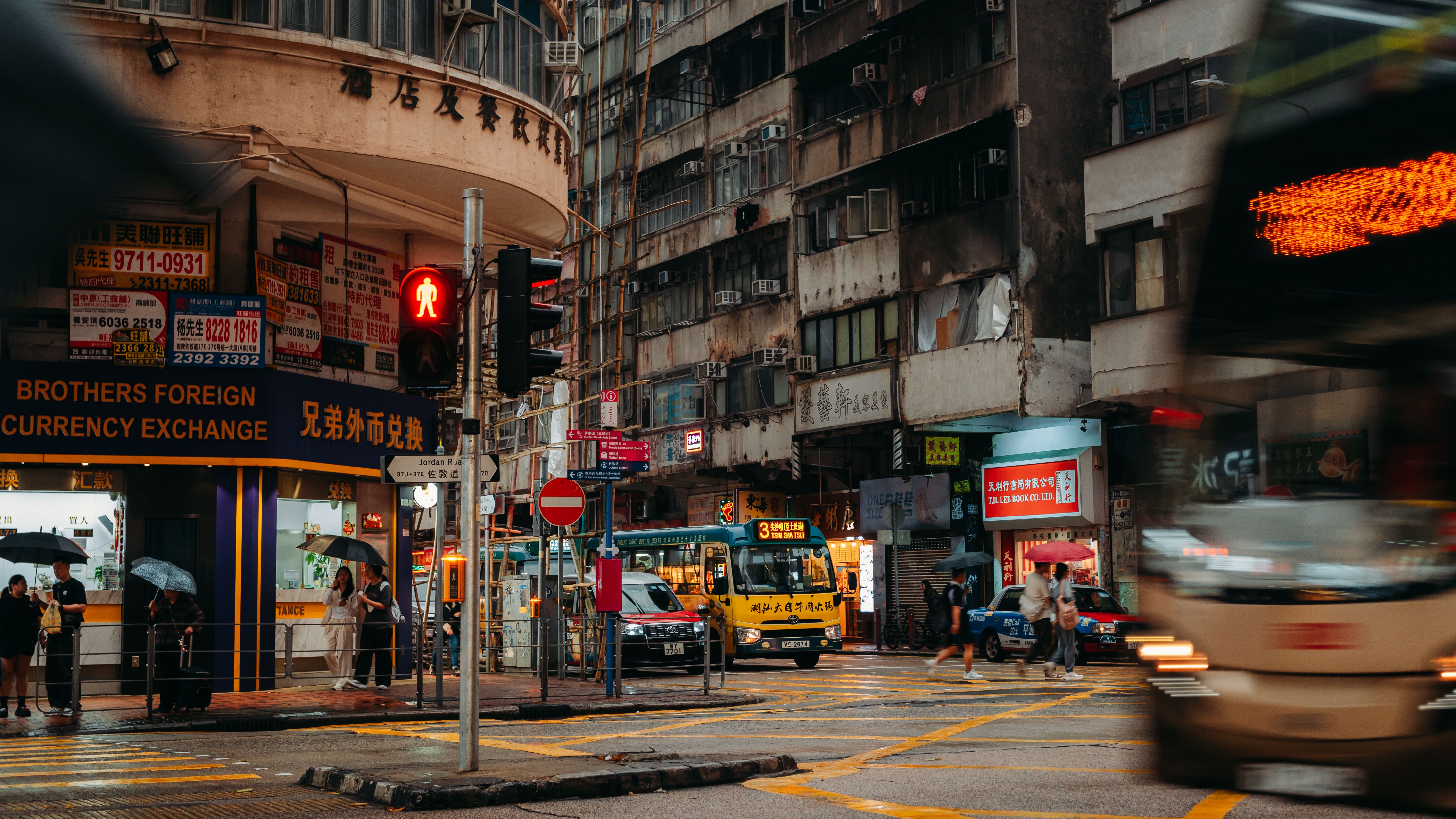 A lively street scene in Hong Kong, showcasing local shops, busy traffic, and pedestrians.