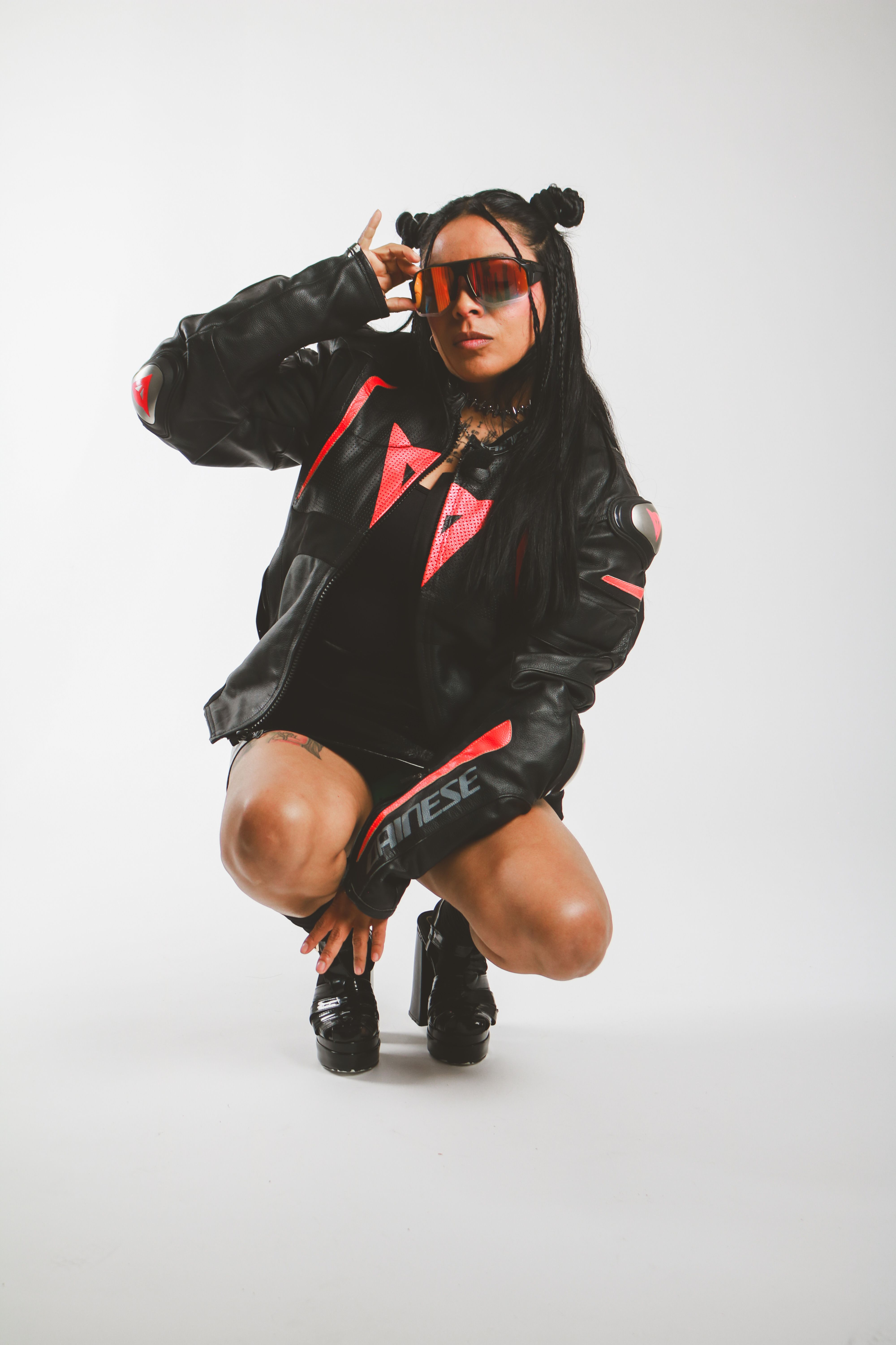 Trendsetting woman squats in leather jacket and cool shades. High-fashion urban style.