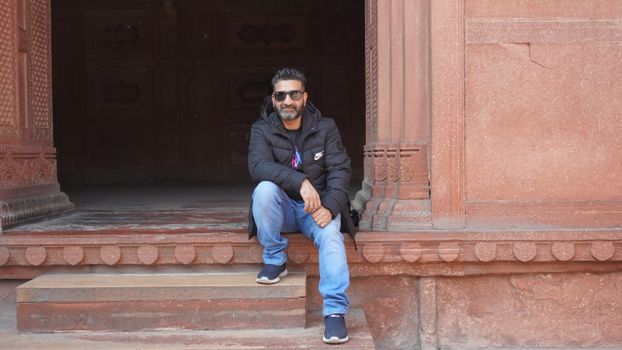 Man sitting on ancient stone steps outdoors, wearing sunglasses and casual attire.