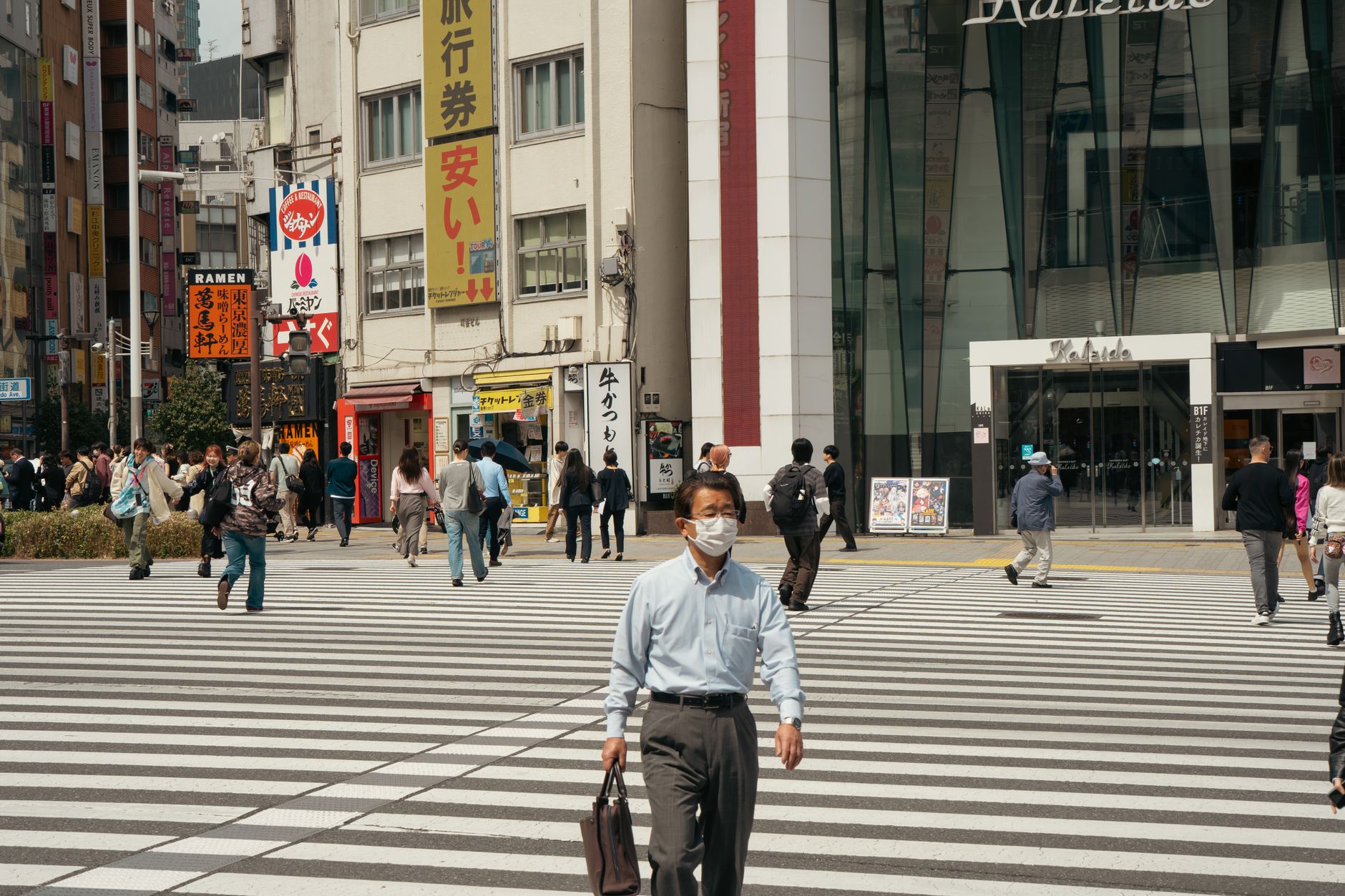People crossing street in Tokyo with tall buildings, showcasing urban life.