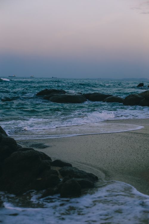 Free Serene twilight scene of ocean waves gently hitting a rocky shoreline on a calm evening. Stock Photo
