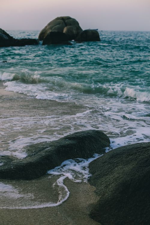 Free A tranquil beach scene featuring gentle waves crashing on rocks with a distant horizon. Stock Photo