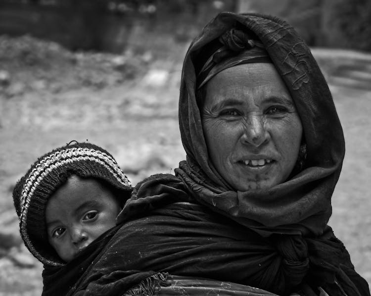 Grayscale Photo Of Woman In Black Hijab Carrying Baby Wearing A Knit Cap