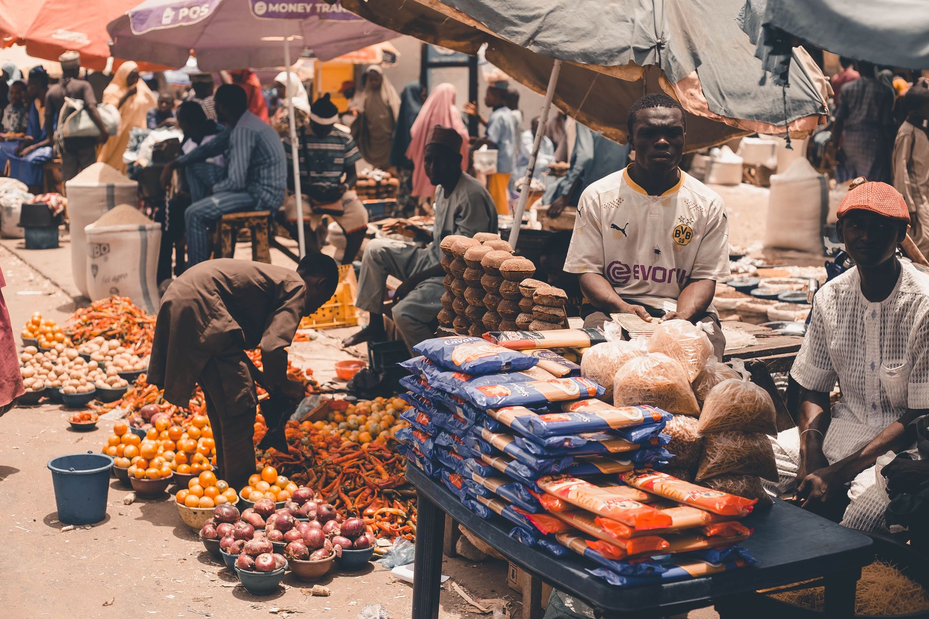 Bustling outdoor African market with vendors selling fresh produce and goods under umbrellas.