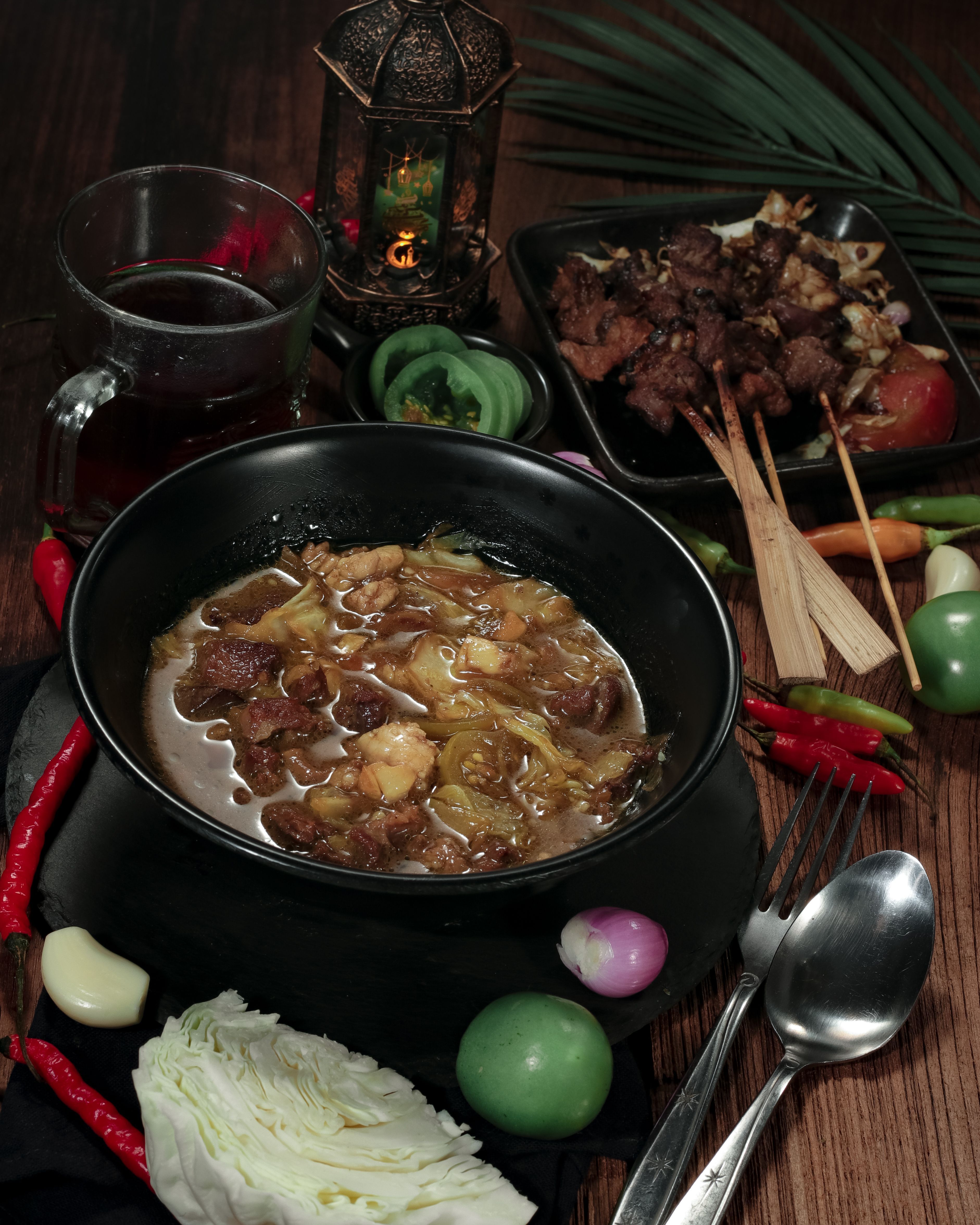 A bowl of rich orange-red Ghanaian palm nut soup with tender pieces of goat meat, wilted green spinach, and whole scotch bonnet peppers floating on the surface
