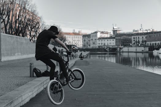 An athlete performs a BMX freestyle trick along a Milano canal on an overcast day.