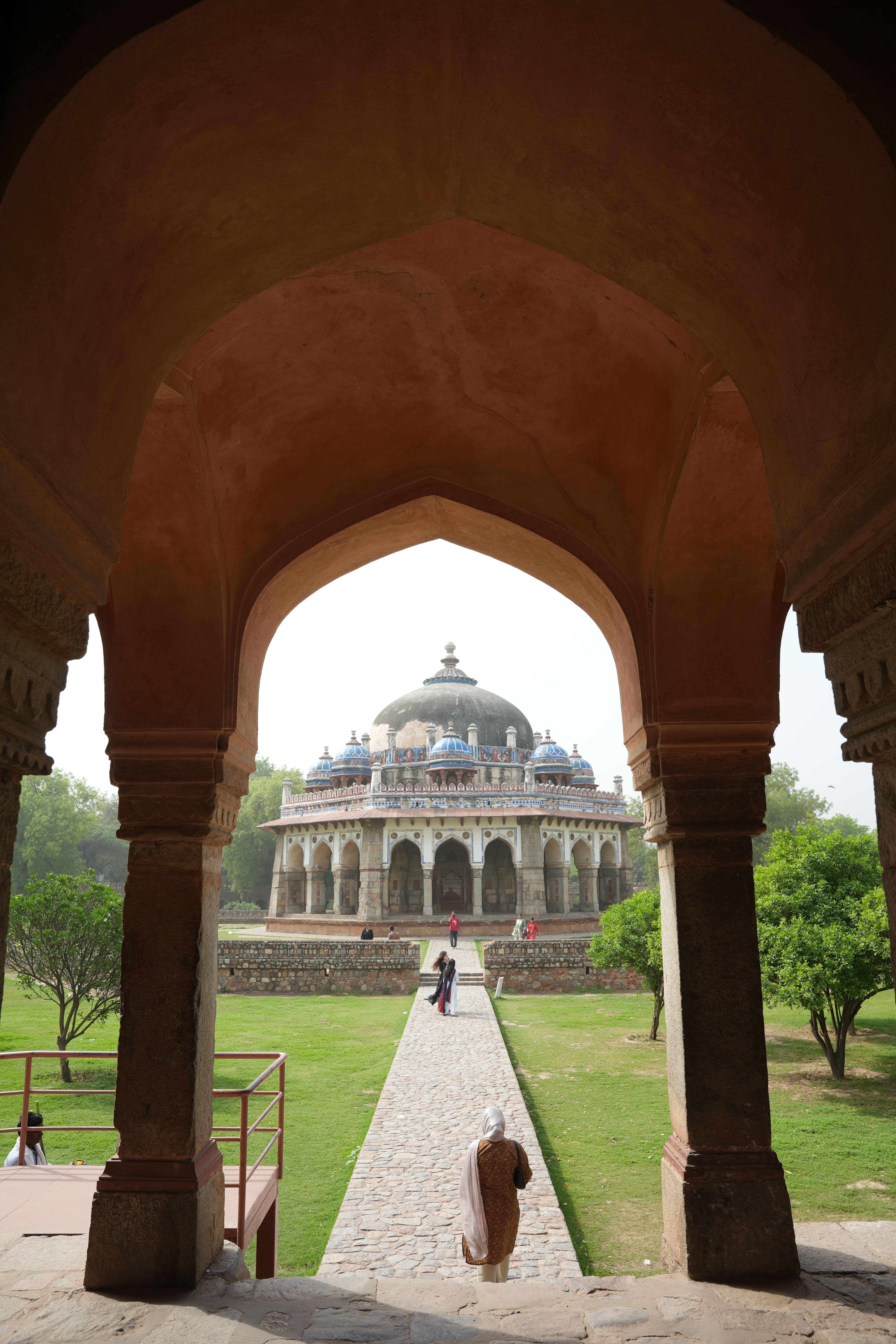 An arch frames the historic Isa Khan's Tomb in a lush garden, captured in New Delhi.