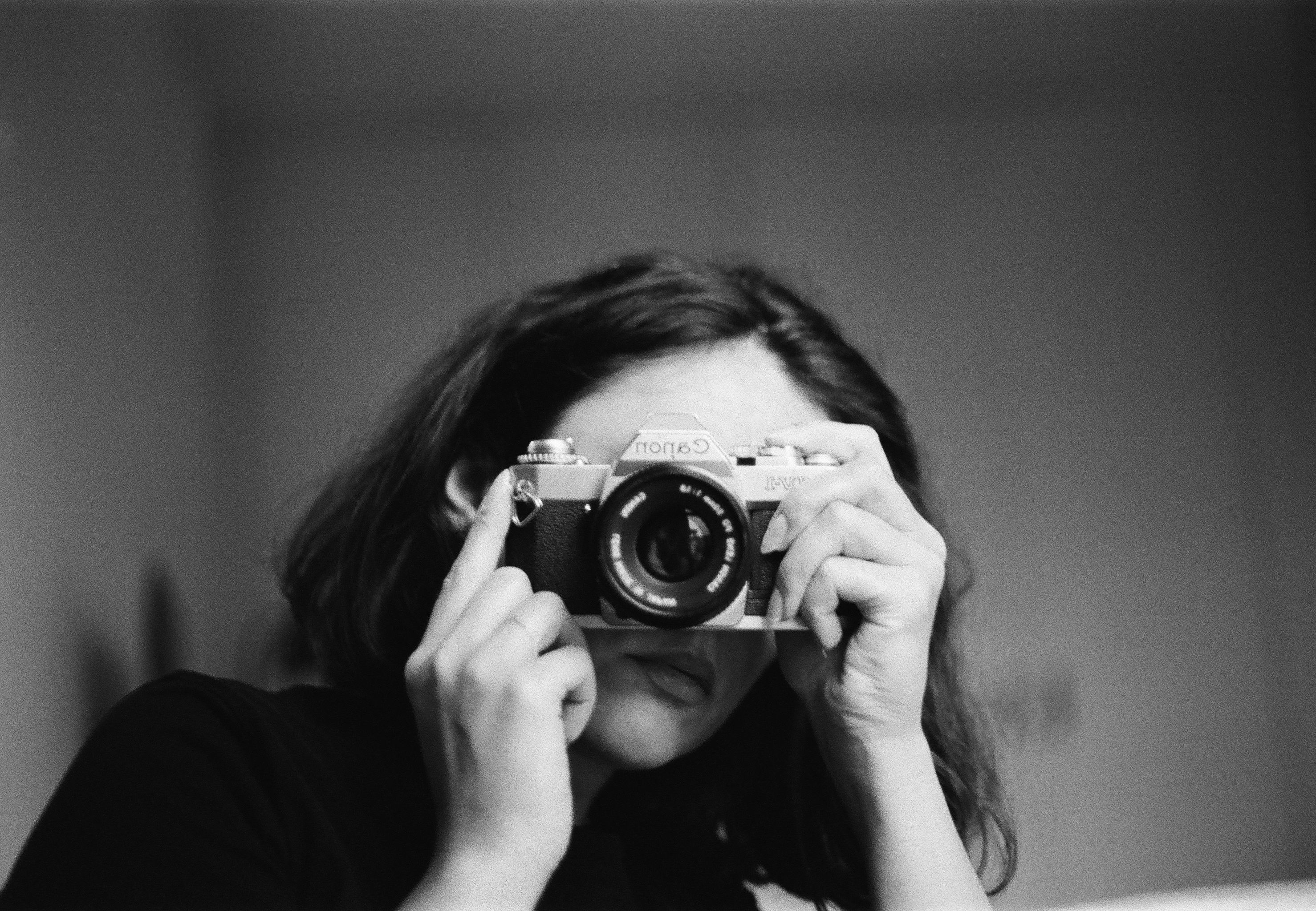 Artistic black and white portrait of a woman holding a vintage camera indoors.