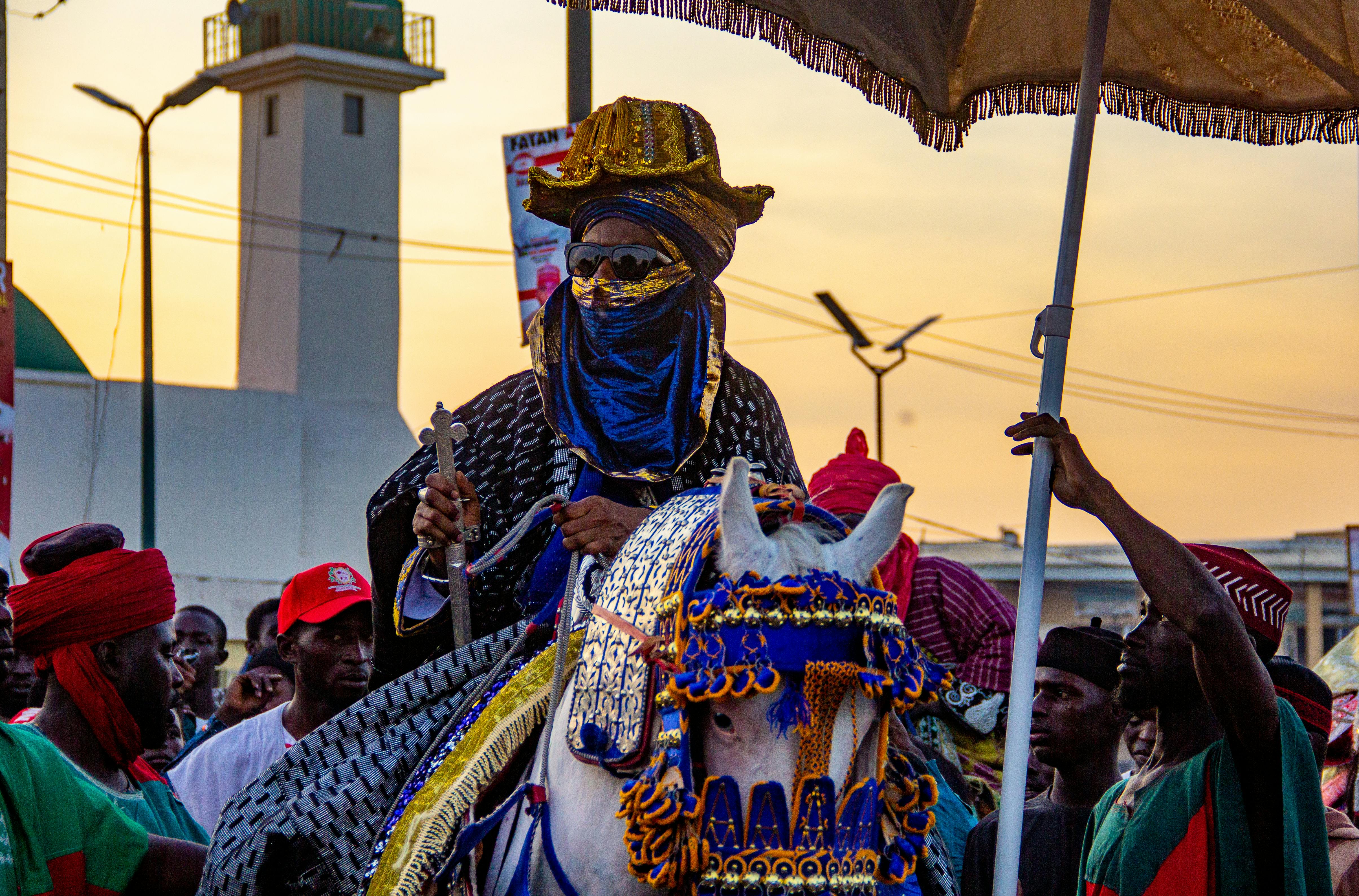 A traditional parade showcasing vibrant attire and mounted riders at sunset.
