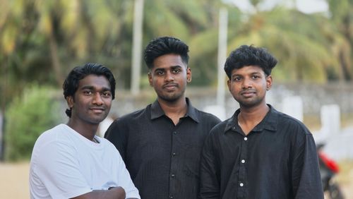 Free Three young men posing together outdoors with a blurred background of trees. Stock Photo