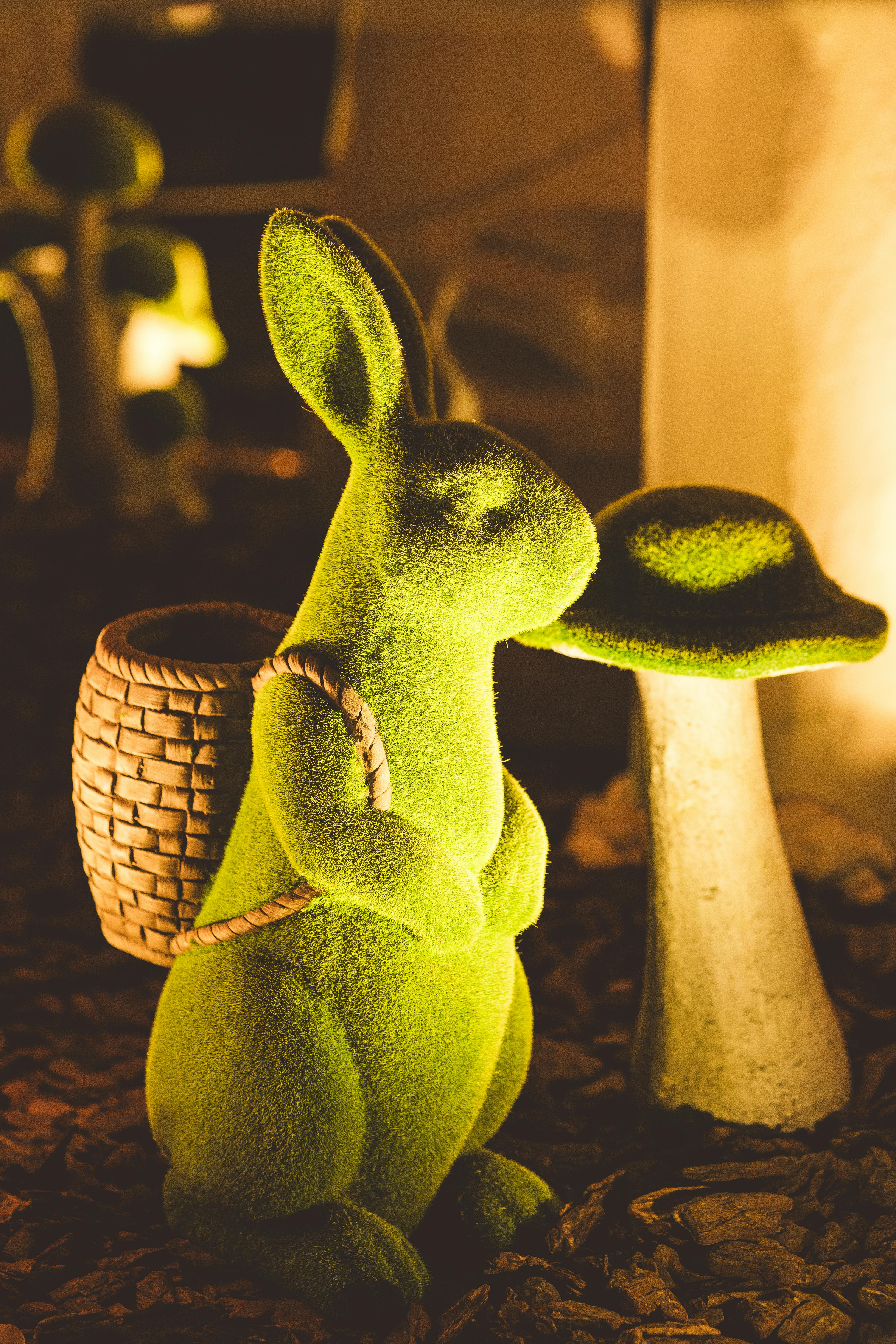 Moss-covered rabbit figure with basket beside a mushroom in a twilight garden scene.