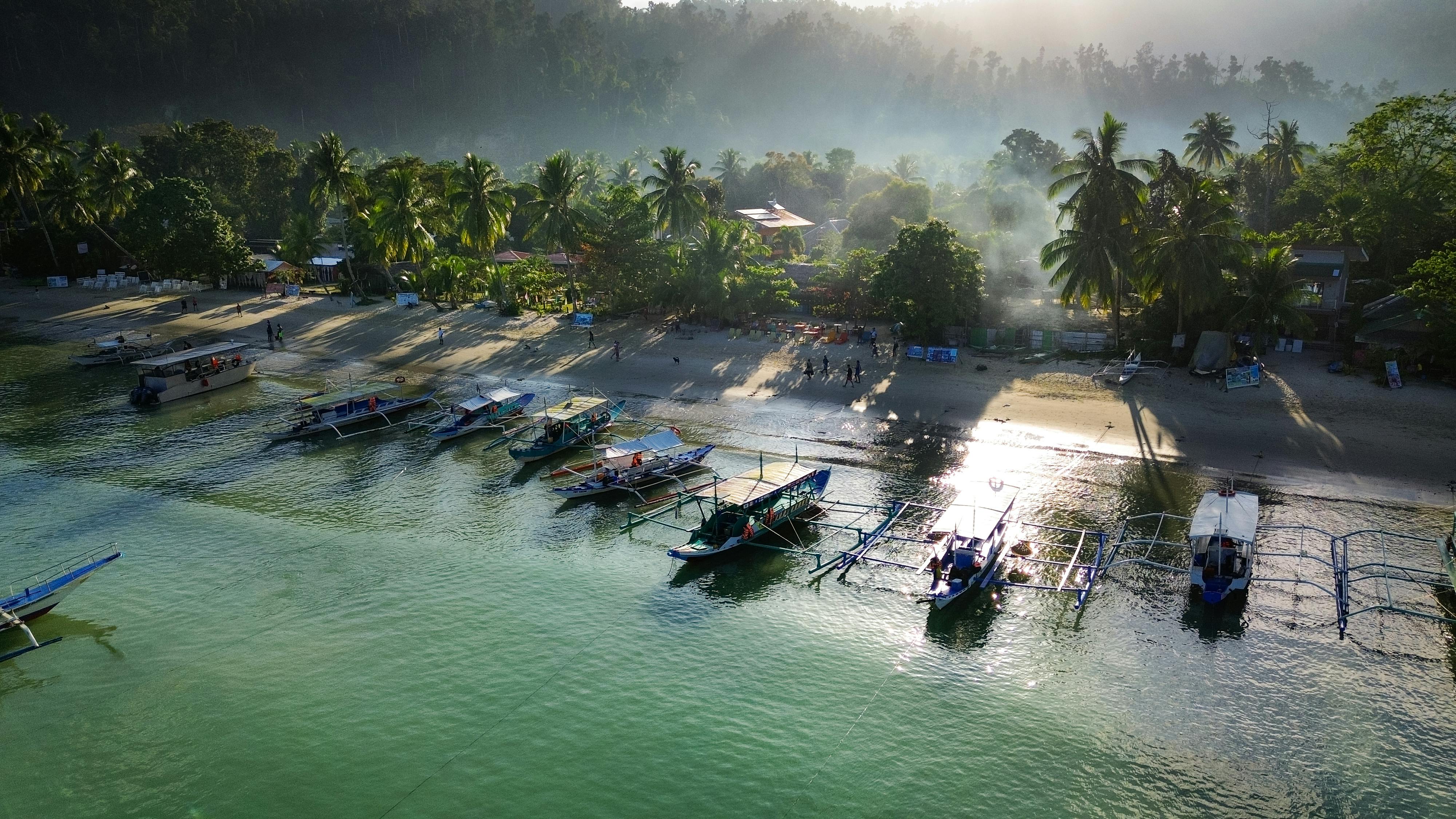 Aerial view of traditional Balinese jukung fishing boats lined up on a turquoise-water beach in Bali at sunrise