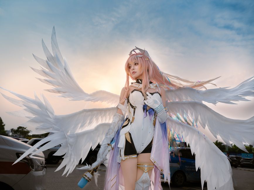 大きな翼を持つ天使のコスプレをした人が、夕暮れ時の屋外に立っている。