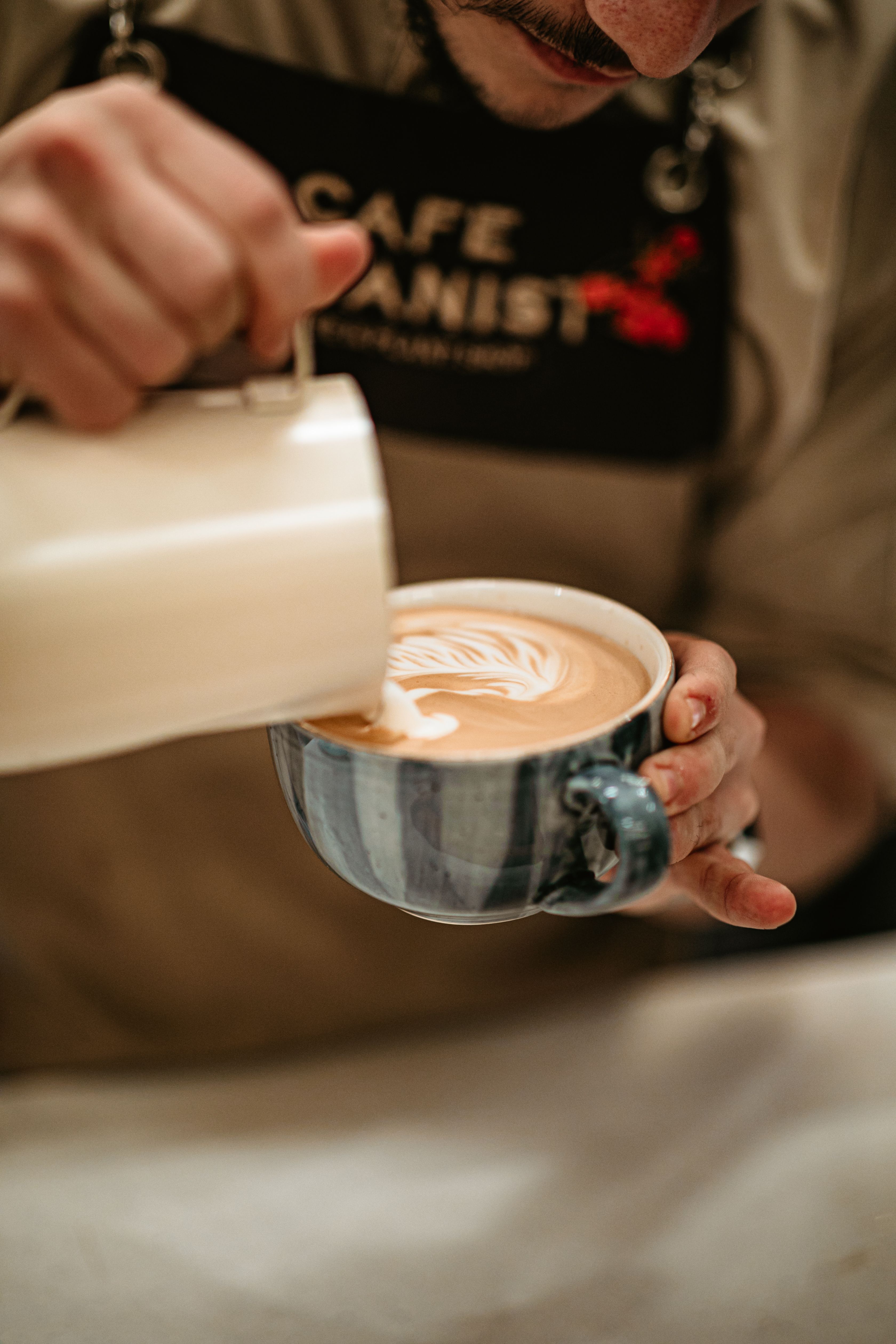 Lait versé d'un pichet dans une tasse tenue à la main, latte art en formation
