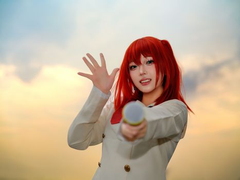 A lively cosplay performer with red hair and microphone at sunset, creating an energetic atmosphere.