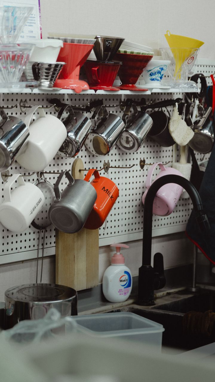 black metal wall-mounted mug rack holding ceramic mugs above a kitchen coffee bar