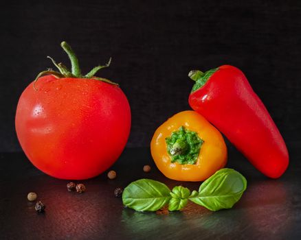 Vivid display of tomato, peppers, and basil on a dark surface, ideal for culinary themes.