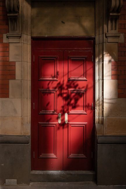 A classic red door in Melbourne with striking shadows and detailed woodwork.