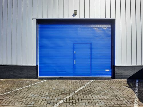 Free Wide shot of a modern industrial warehouse featuring a bright blue garage door. Stock Photo