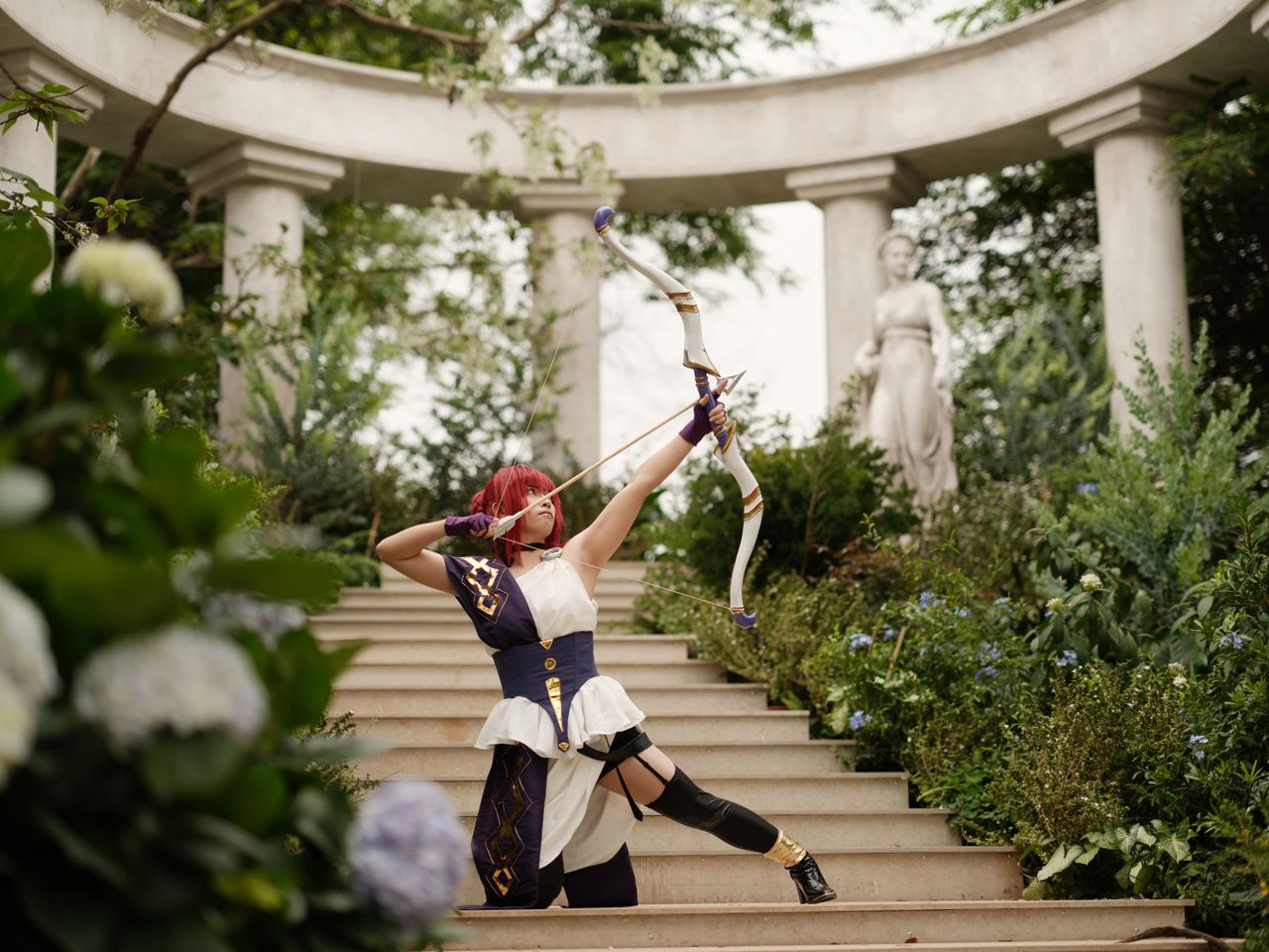 cosplayer in archer attire performs dynamic pose in a serene garden wi