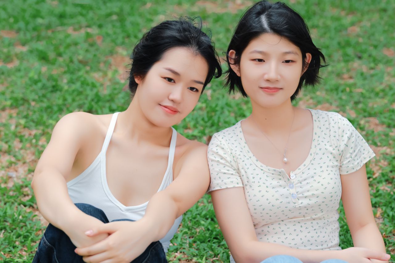two young women sitting on grass enjoying a sunny day outdoors