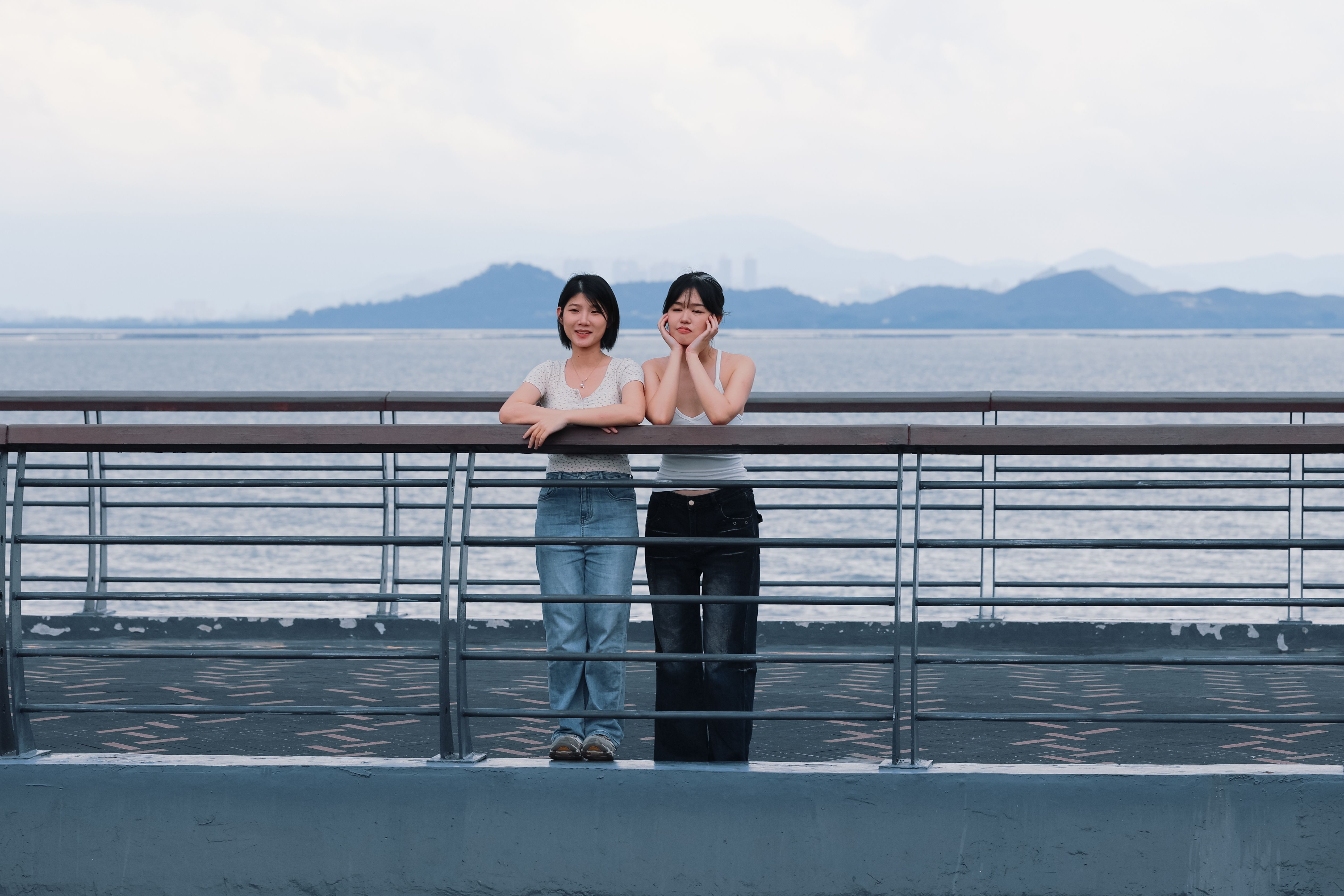 Two Friends Standing by Waterfront Railing · Free Stock Photo
