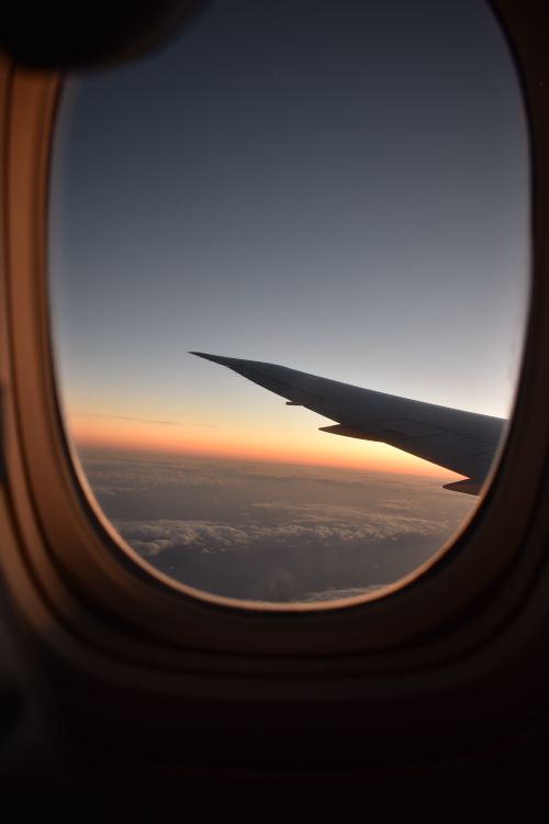 Free Capture of an airplane wing viewed through the cabin window, showcasing a stunning sunrise above the clouds. Stock Photo