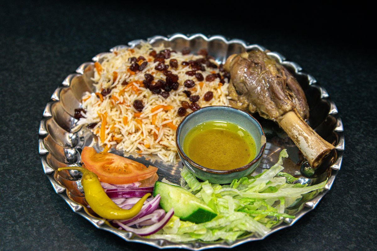 Pulao rice with carrots and raisins, lamb shank, salad and oil dip on a silver platter