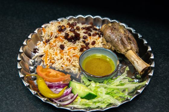Pulao rice with carrots and raisins, lamb shank, salad and oil dip on a silver platter
