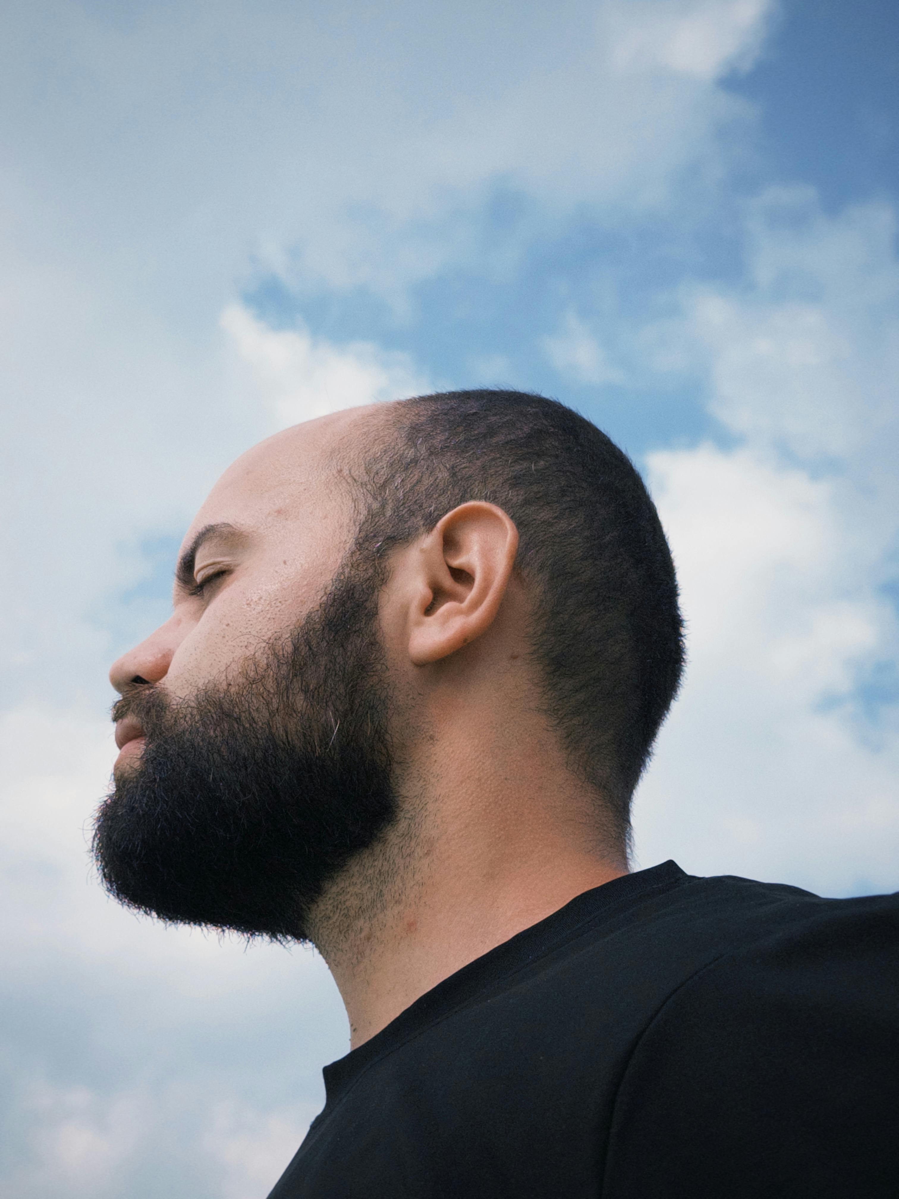 Profile of a bearded man looking up at a cloudy sky, capturing a contemplative moment outdoors in Paraná, Brazil.