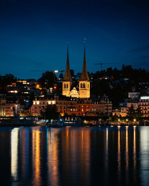 Free A stunning night view of Lucerne's waterfront reflecting lights, featuring iconic twin-spired church. Stock Photo