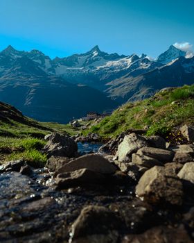 A breathtaking view of a mountain stream flowing through a rocky landscape with snow-capped peaks in the background.