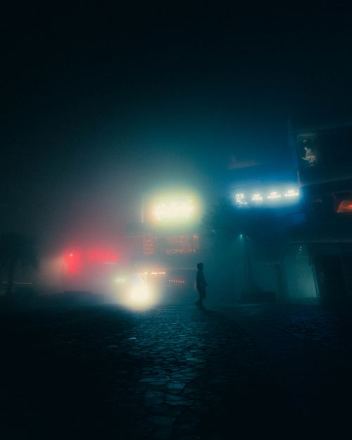 Free A mysterious silhouette walking in a foggy street illuminated by colorful neon lights. Stock Photo