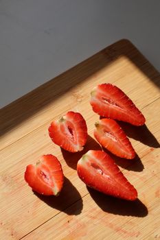Bright red strawberries cut in halves on a wooden board, bathed in natural light.