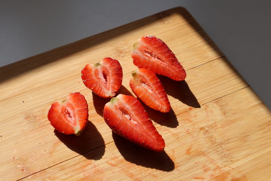 Sliced strawberries on a wooden cutting board with natural light highlighting their texture.