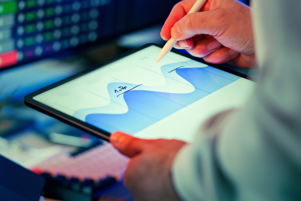 Professional analyzing a data chart on a tablet with a stylus in an office setting.